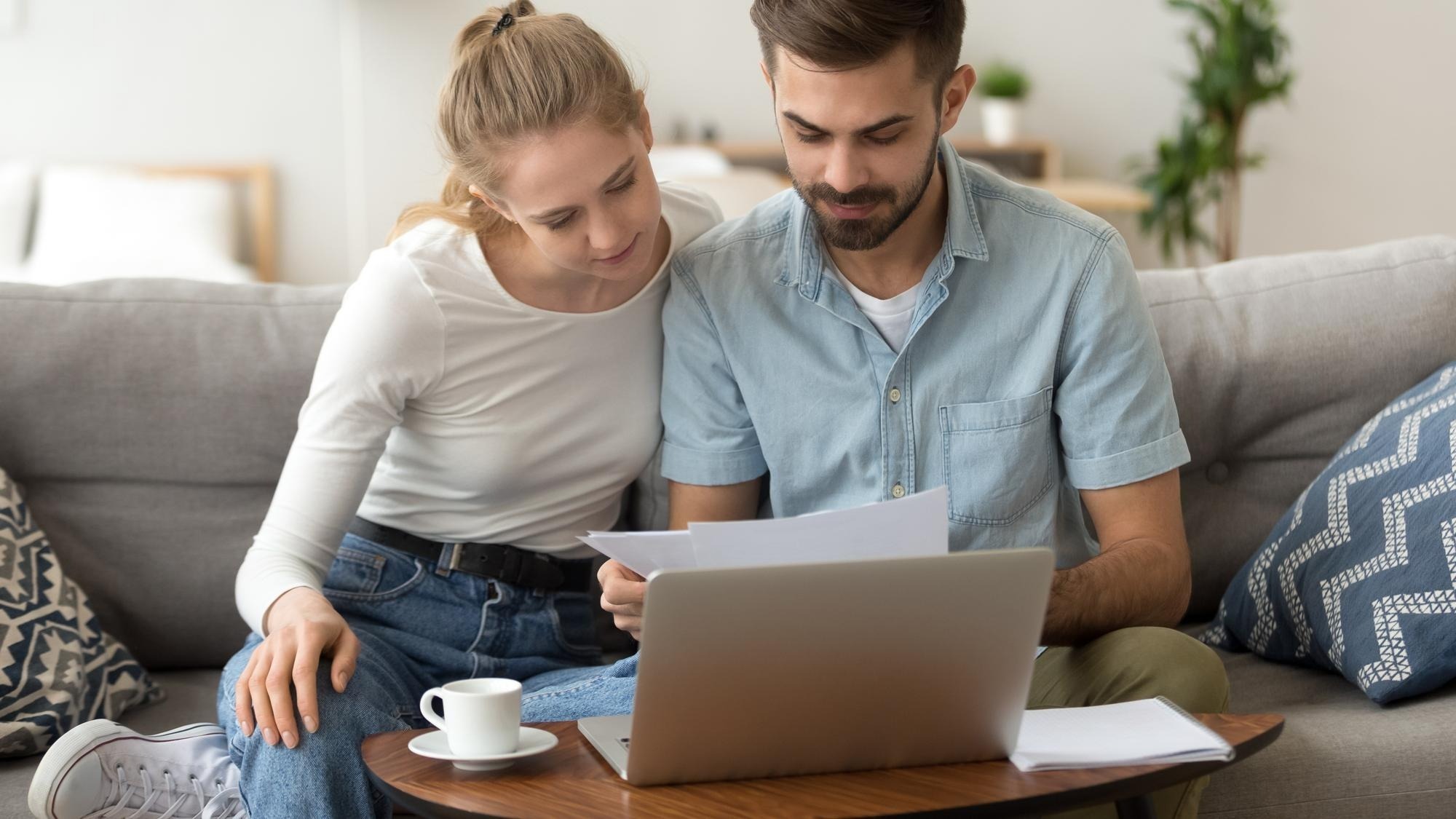 Young serious couple reading financial documents checking bills with laptop