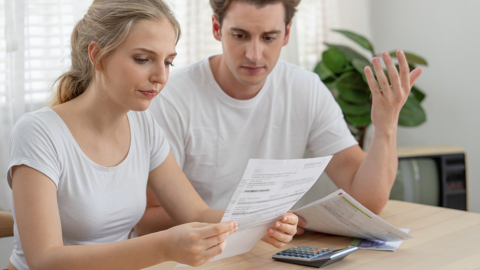 Stressed couple young family financial troubles sitting in living room at home and holding expenses bills from the bank, woman worried on money to pay a debt. Financial problems concept.