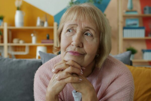 Elderly woman with hands clasped, looking thoughtful