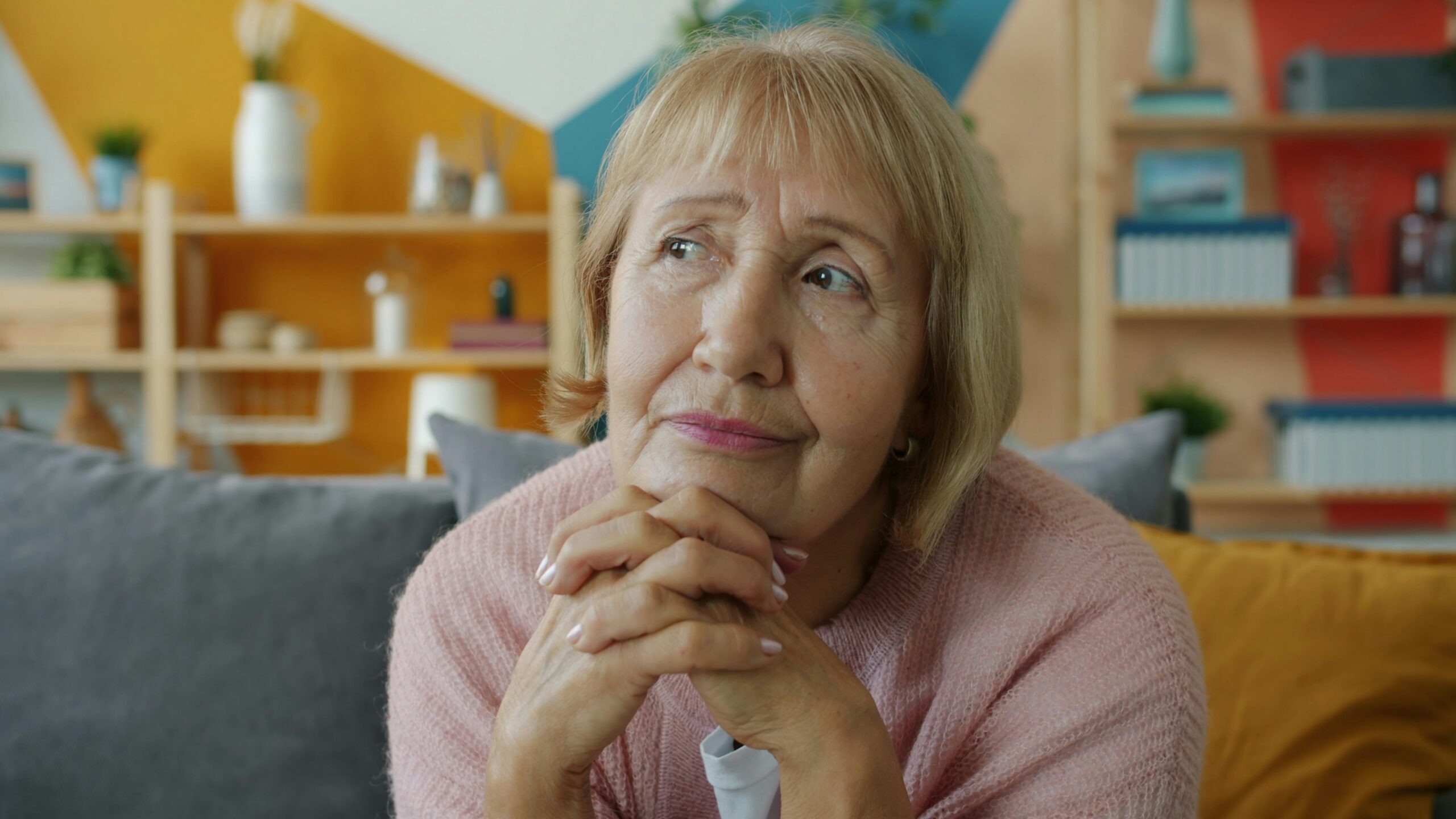 Elderly woman with hands clasped, looking thoughtful