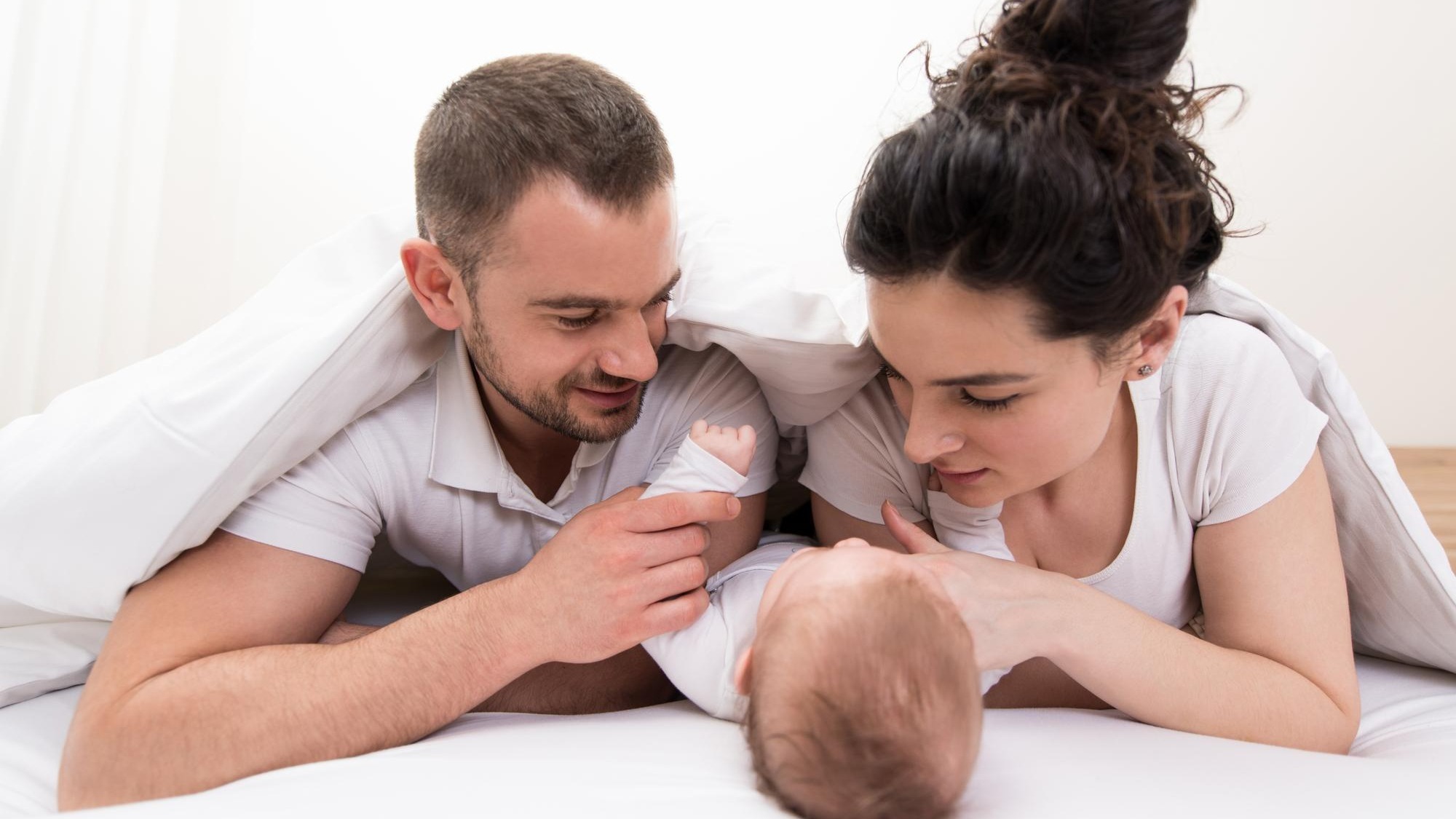 Family With Baby in Bed Under a Blanket