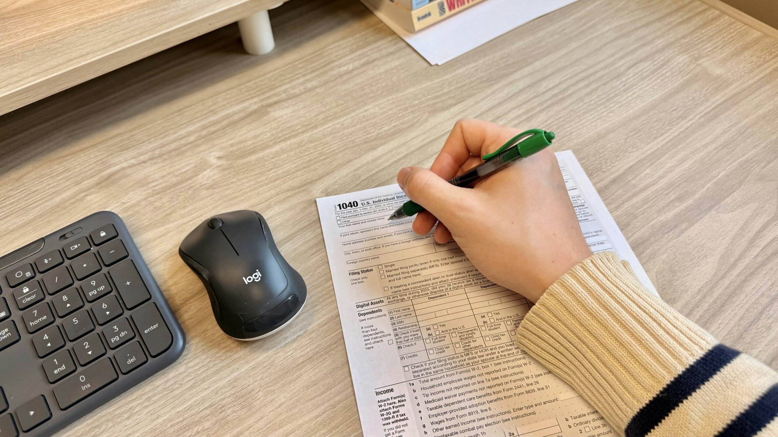 Hand writing on document next to keyboard and mouse