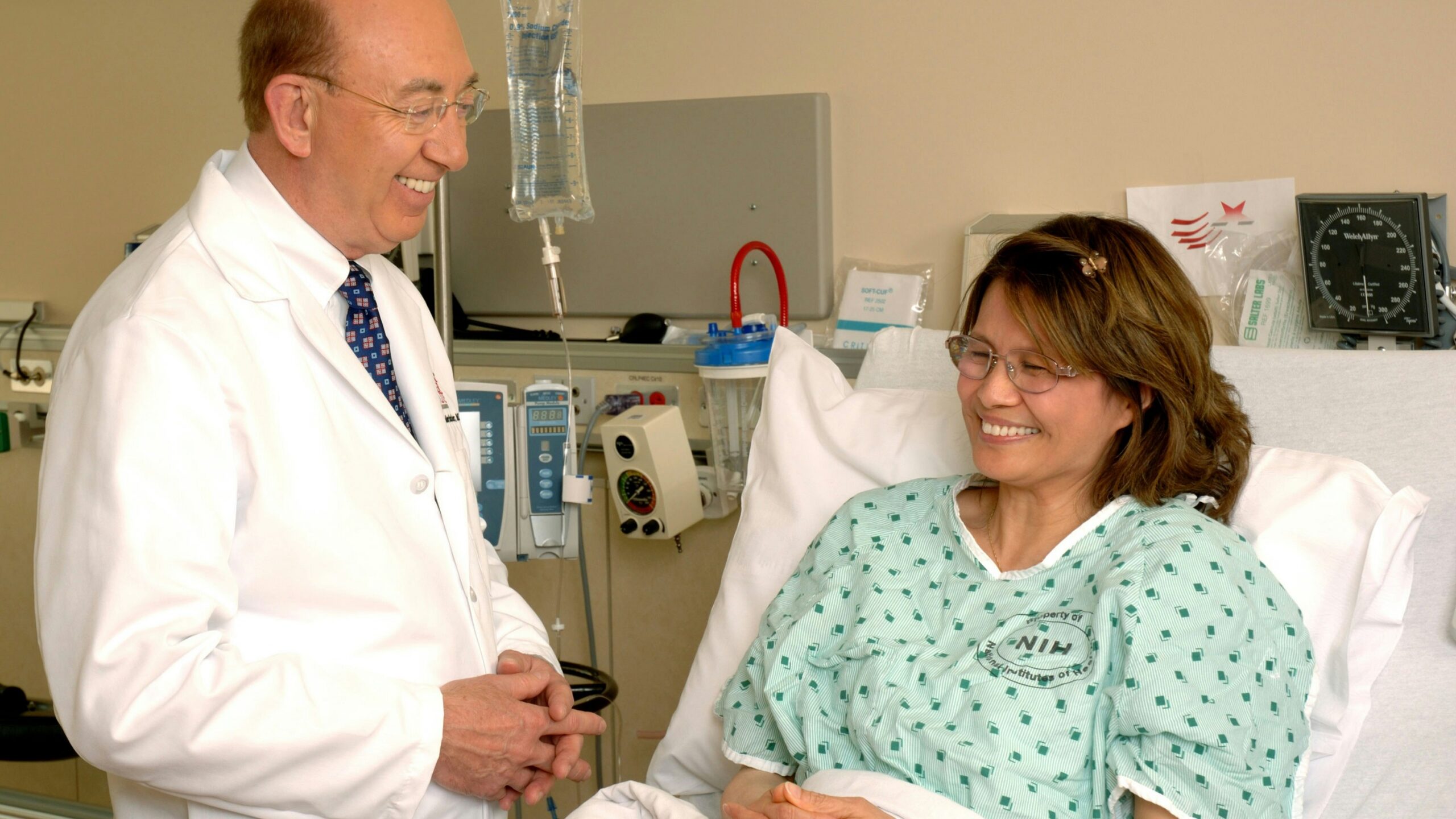 A doctor in a white coat talking to a patient in a hospital bed