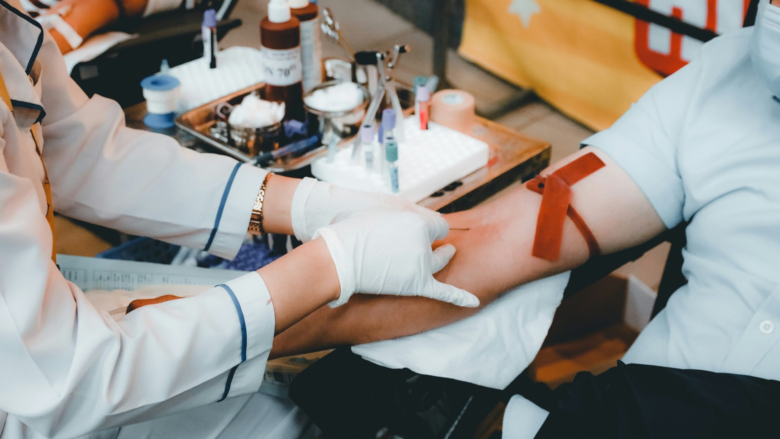 A healthcare worker in white gloves drawing blood from a person's arm