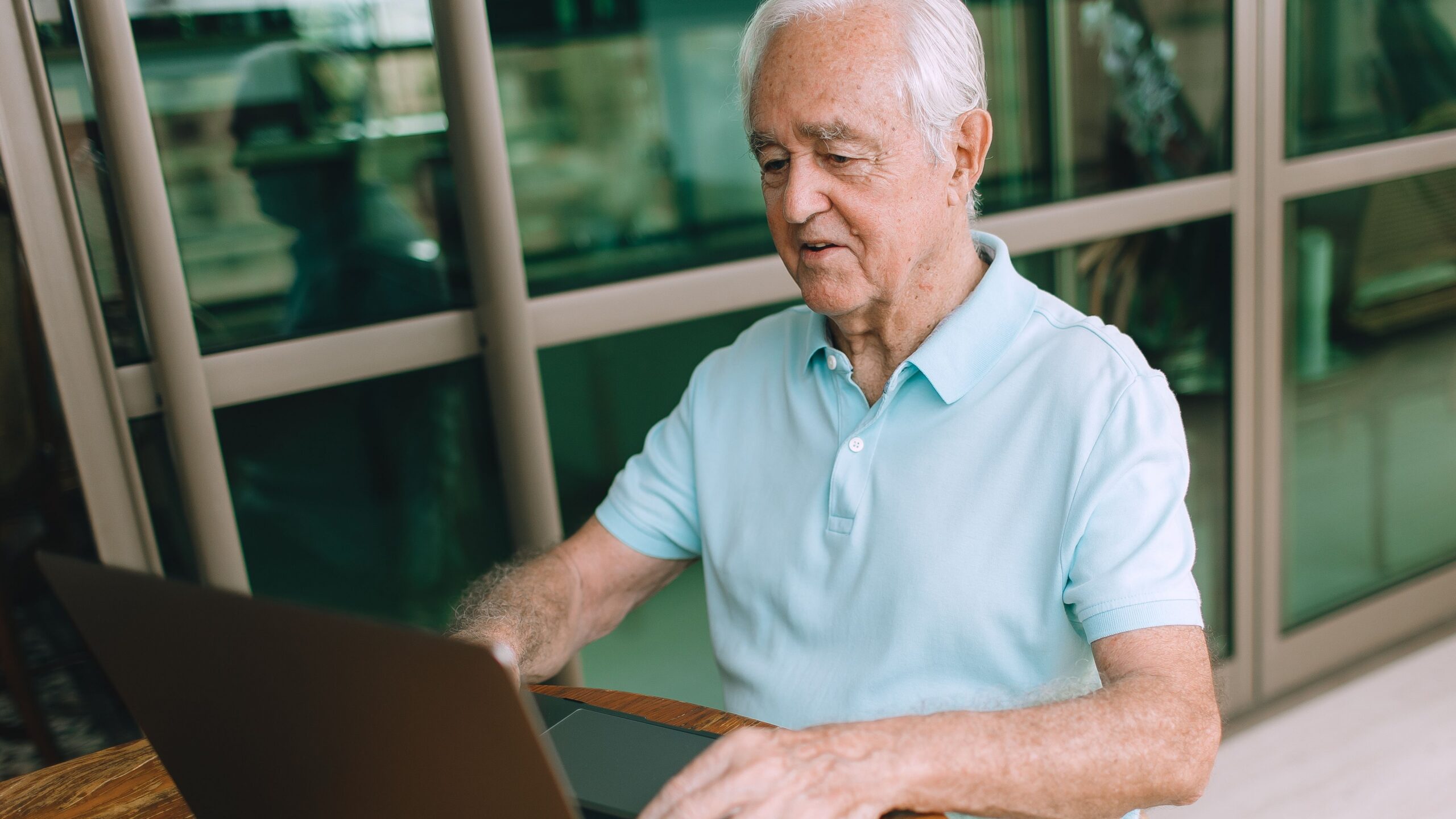 Elderly man enjoying technology, typing on laptop indoors.
