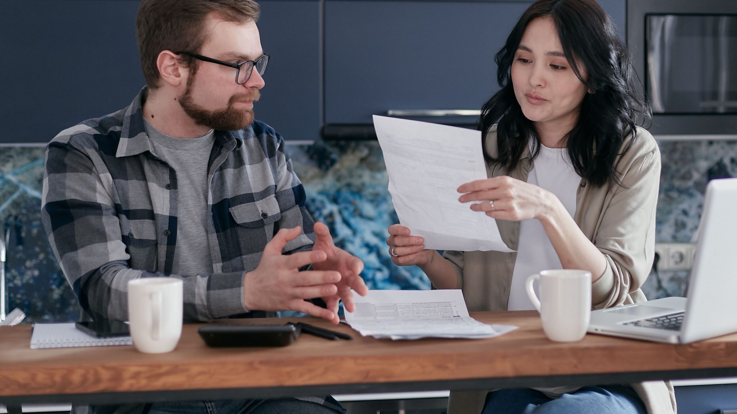 Young couple managing their finances with laptop and documents in a modern kitchen setting.