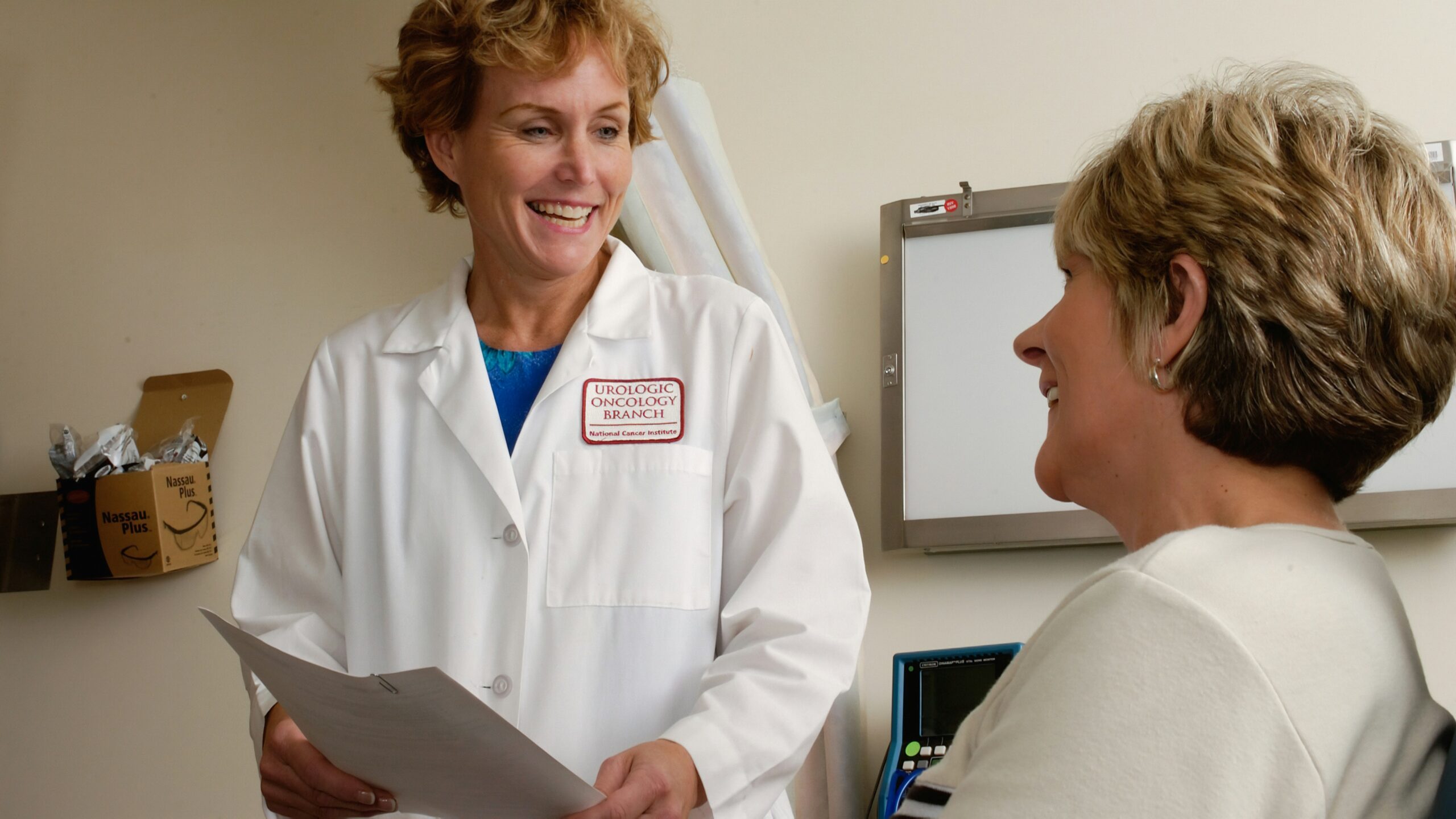 A smiling doctor in a white coat talking to a patient in a clinic