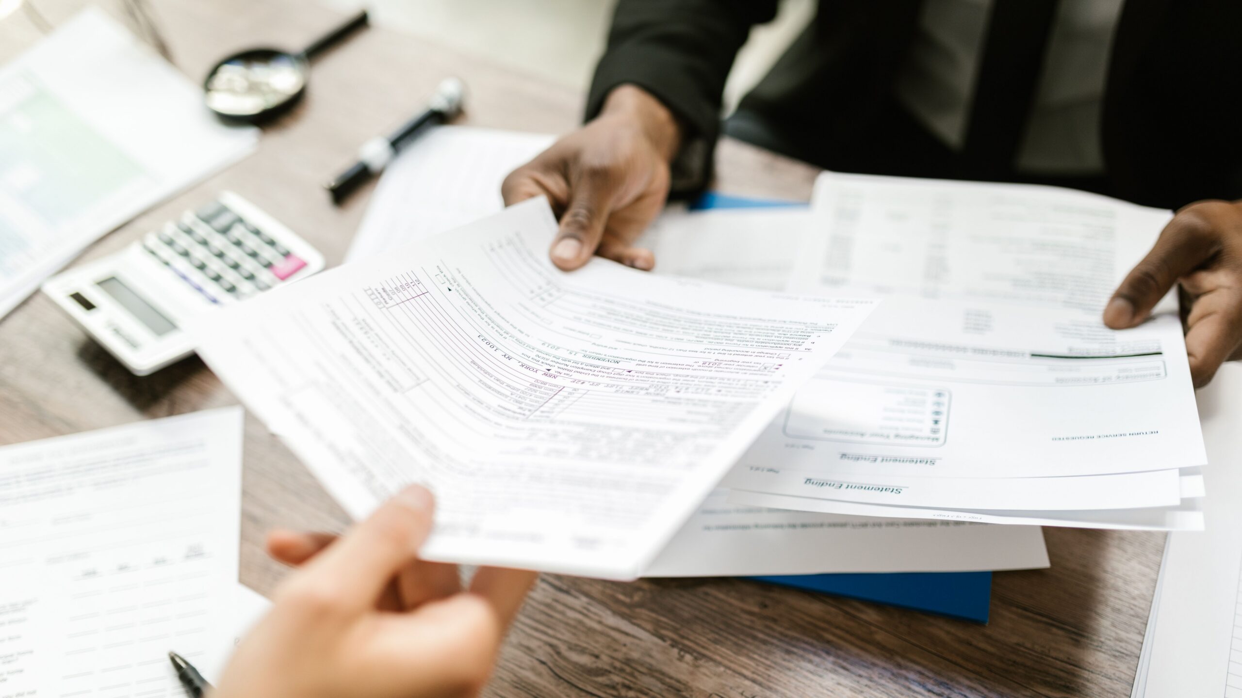 Two professionals exchanging documents in an office setting, focusing on paperwork and data analysis.