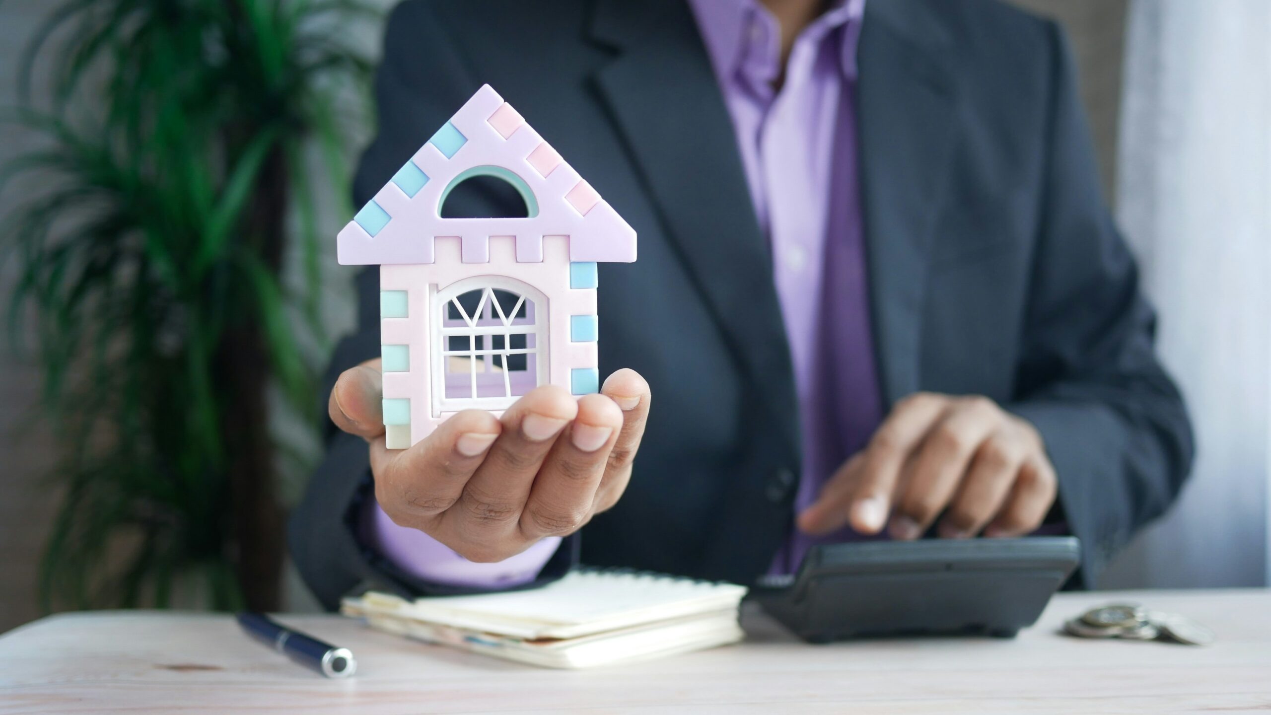 man holding model house at desk with calculator