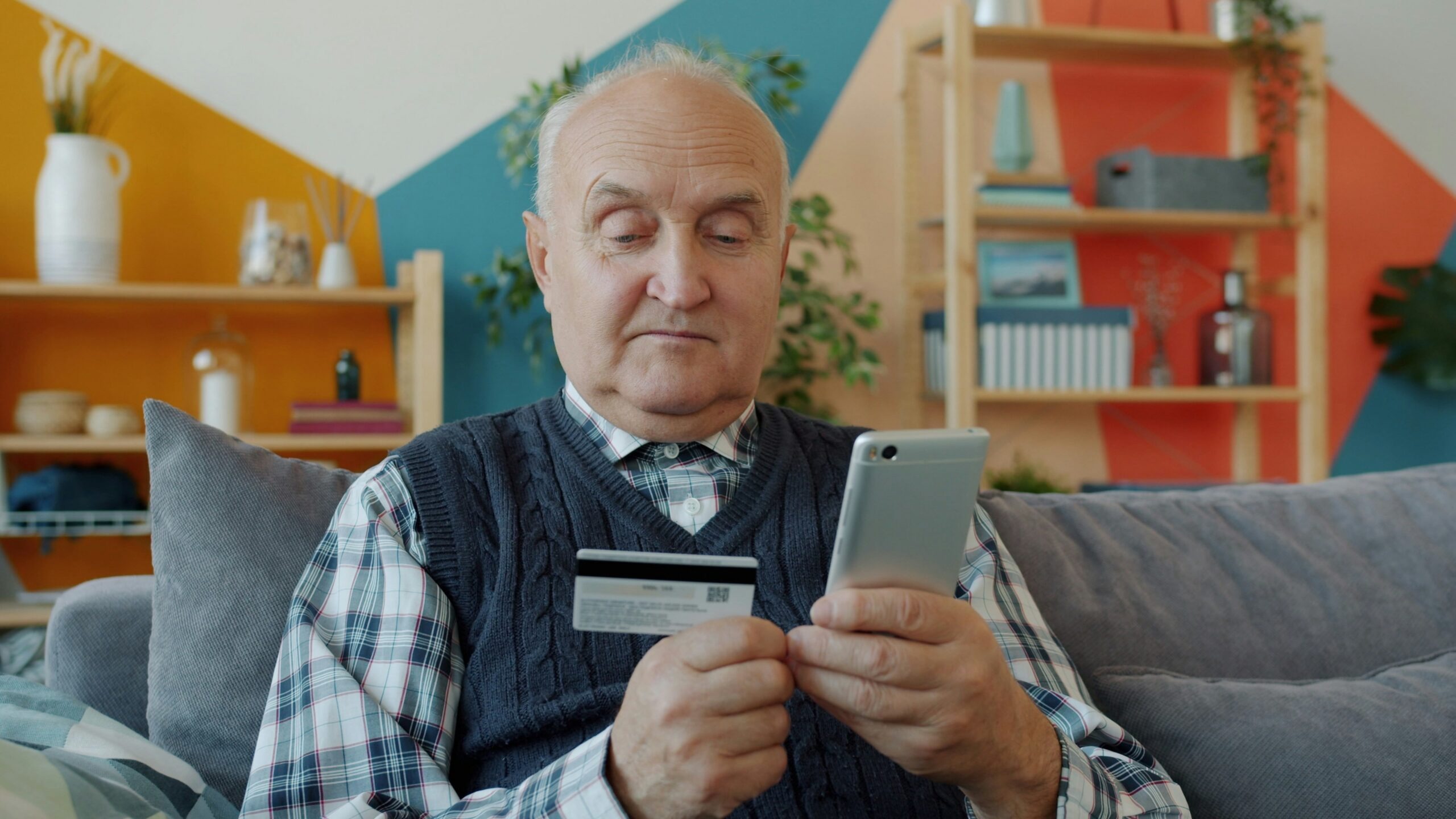 Elderly man holding credit card and smartphone for online shopping.