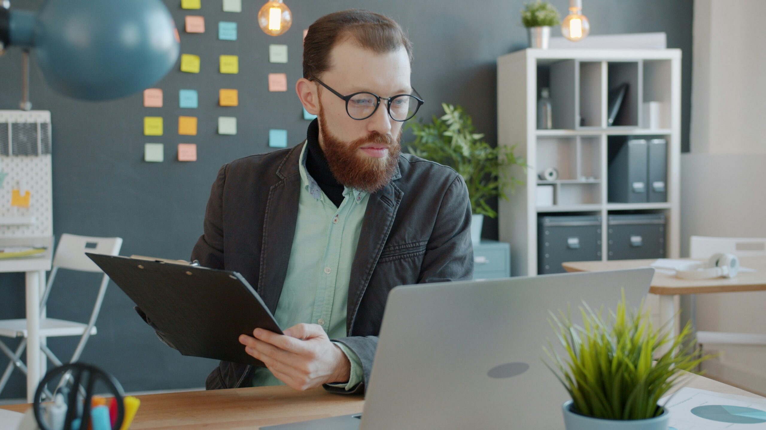 Man with beard working on laptop and clipboard