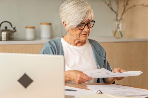 Middle aged senior woman sit with laptop and paper document pensive older mature lady reading paper