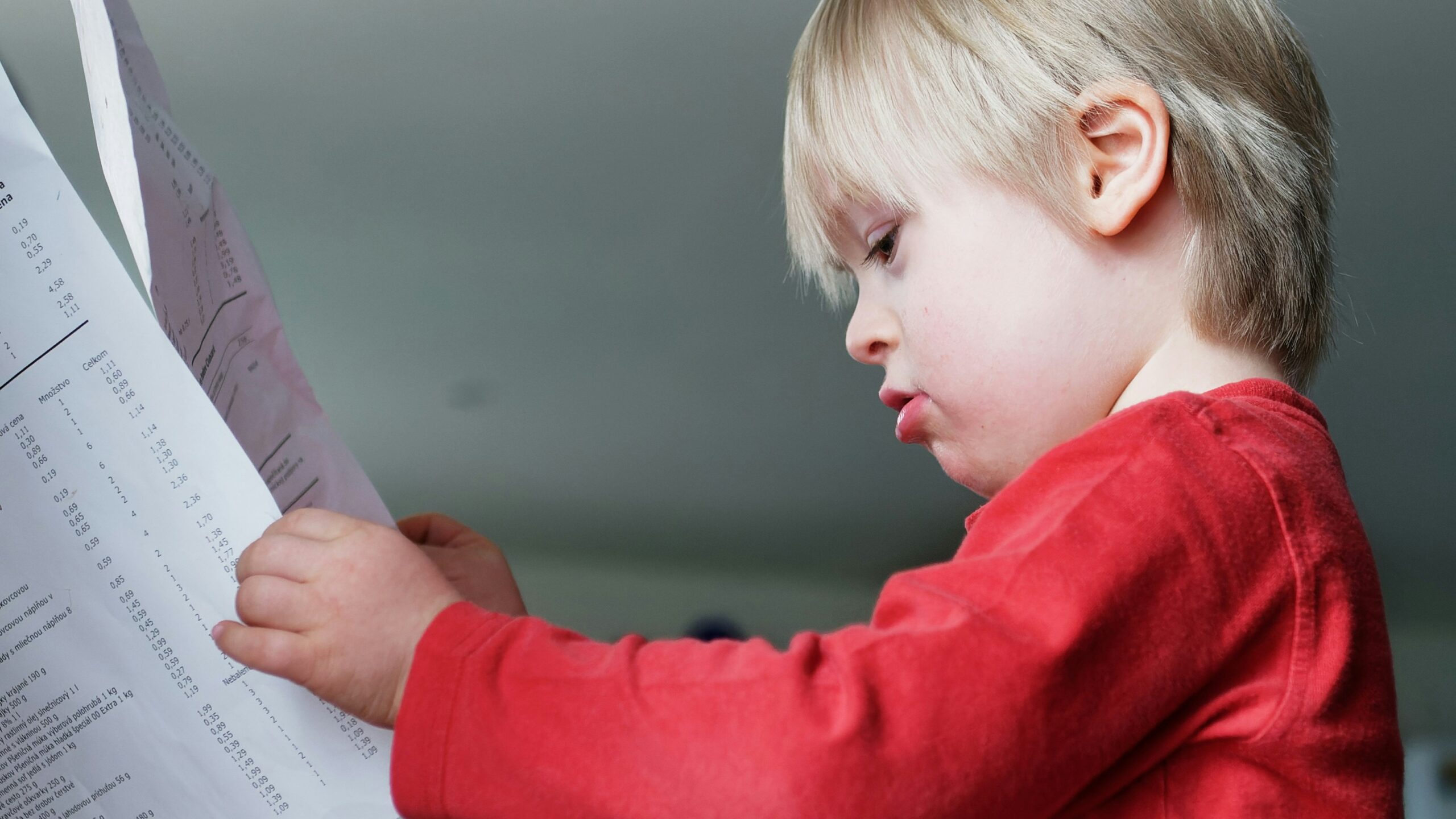 a young boy reading a paper while sitting at a table