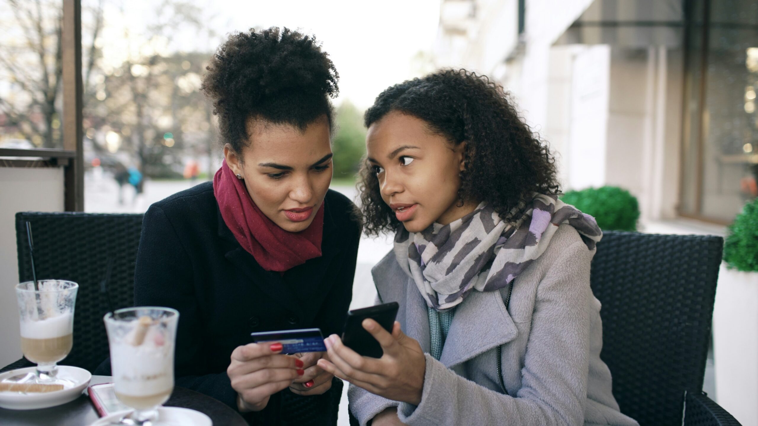Two women looking at a smartphone with credit card
