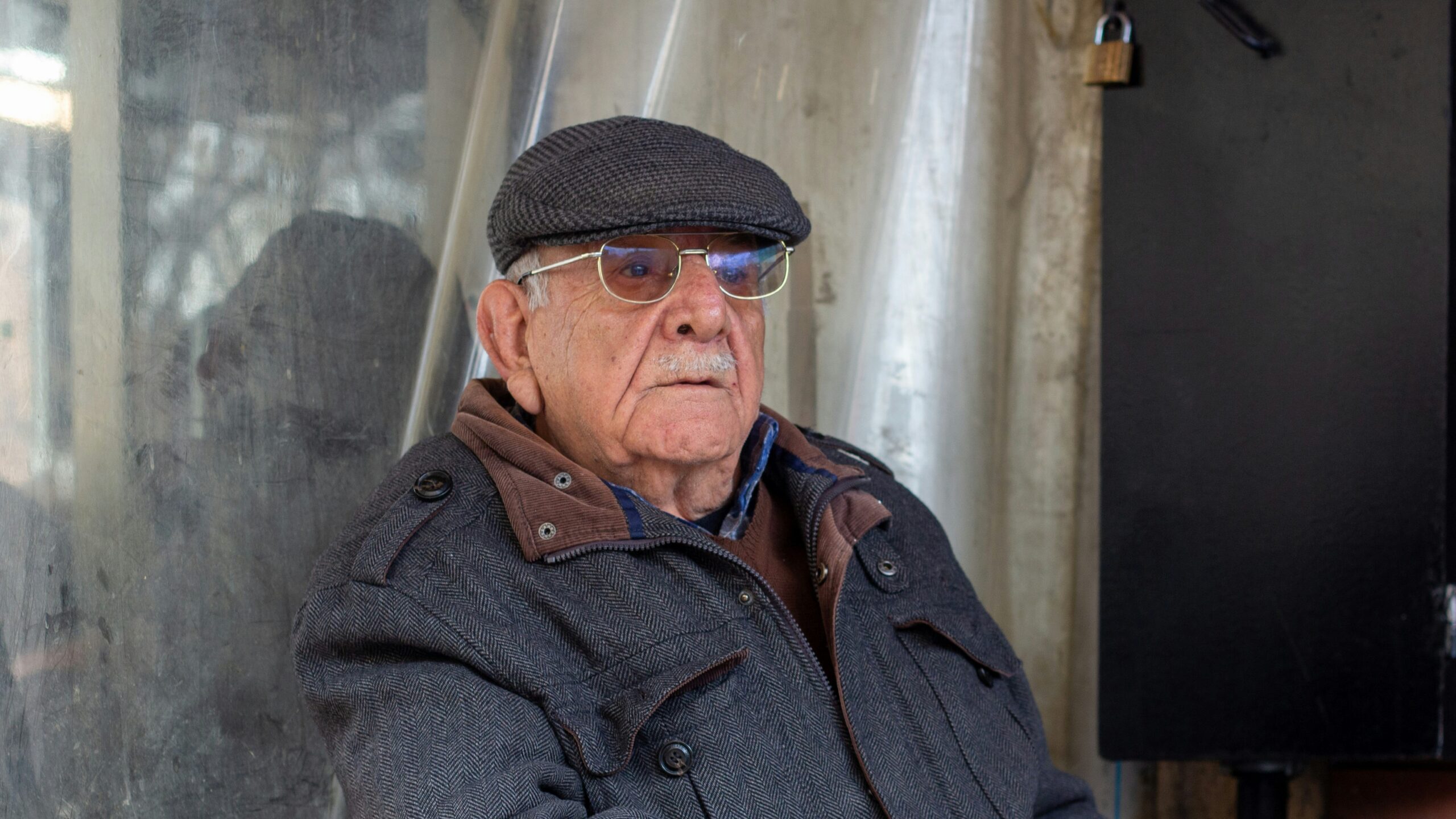 An elderly man in a grey flat cap and jacket at a cafe table