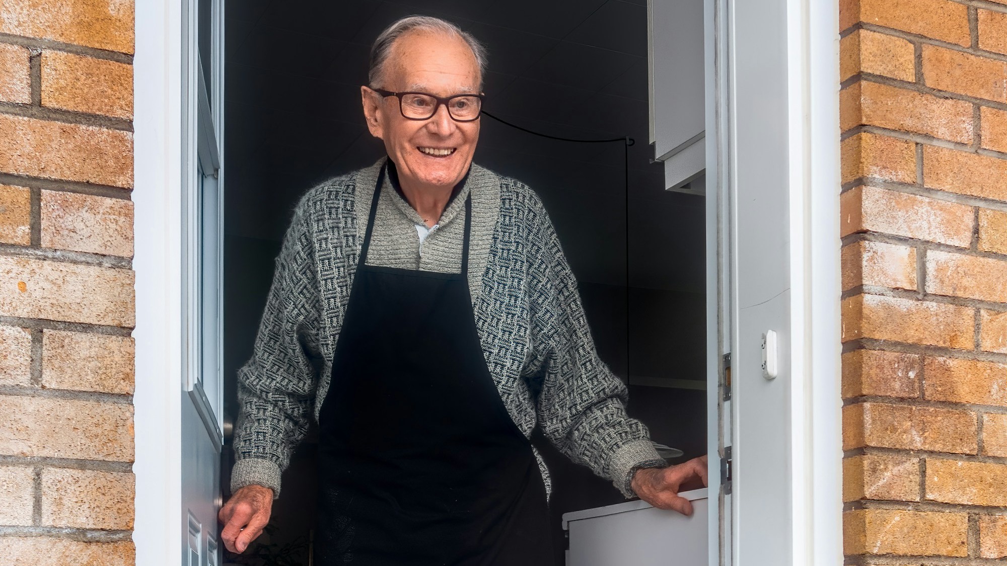 man in black vest and black dress pants standing beside white wooden door
