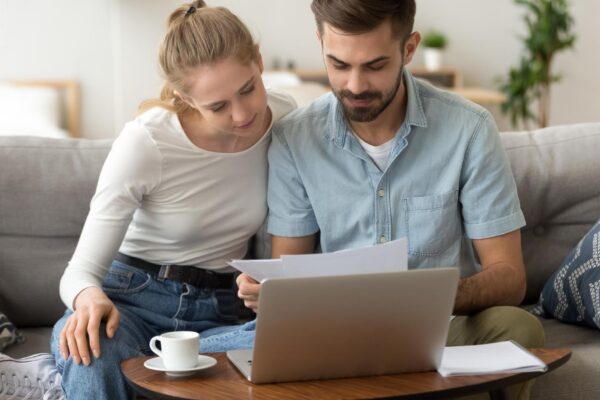 Young serious couple reading financial documents checking bills with laptop