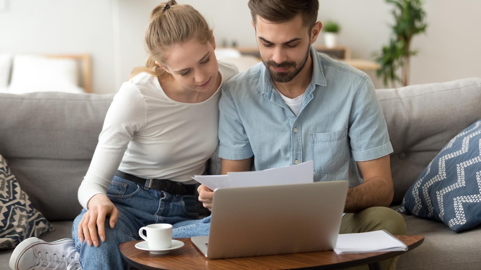 Young serious couple reading financial documents checking bills with laptop