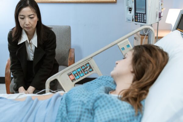 A hospital room showing a patient in bed and a visitor sitting beside her.