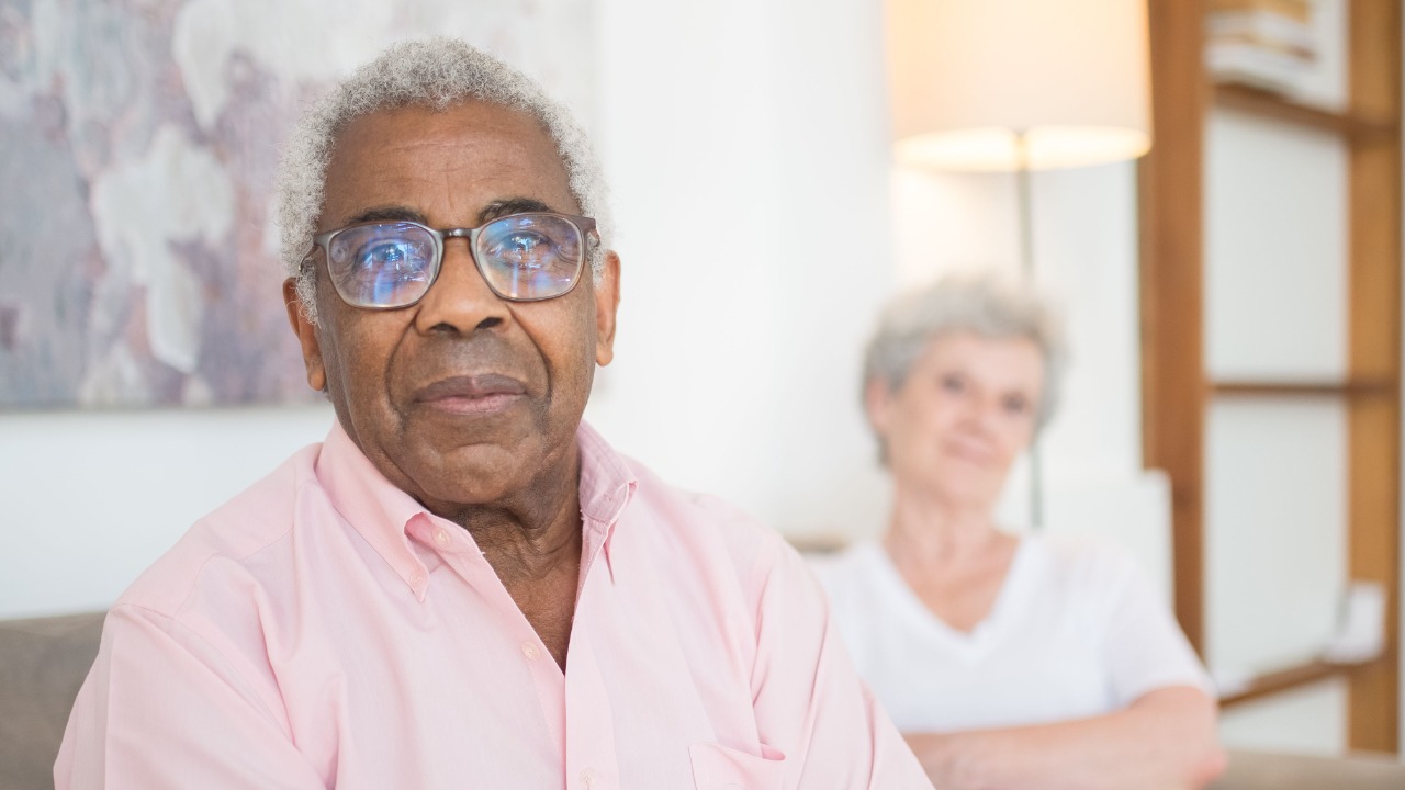 Senior adults relaxing with arms crossed on a couch in a cozy home setting.