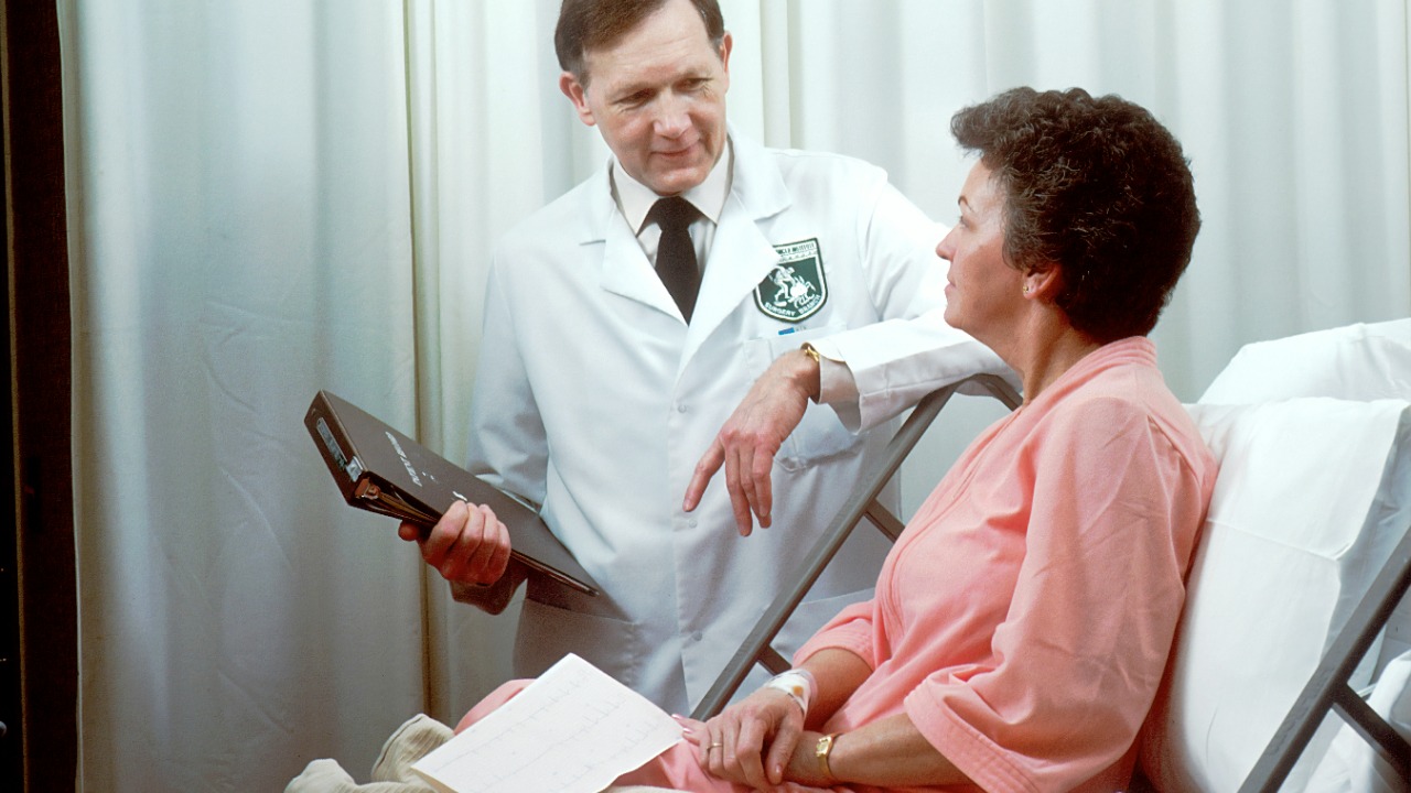 A doctor in a white coat talking to a patient in a hospital bed