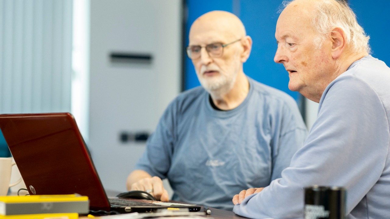 two men sitting at a table looking at a laptop