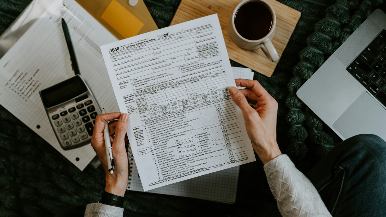 Hands holding tax forms with calculator and laptop