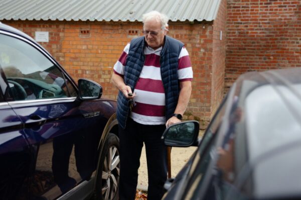 An older man stands between two cars