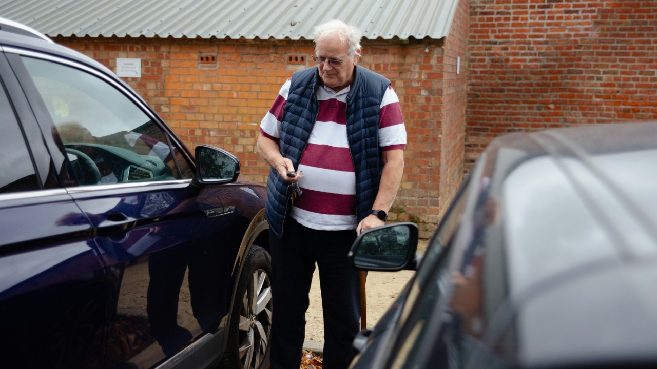 An older man stands between two cars