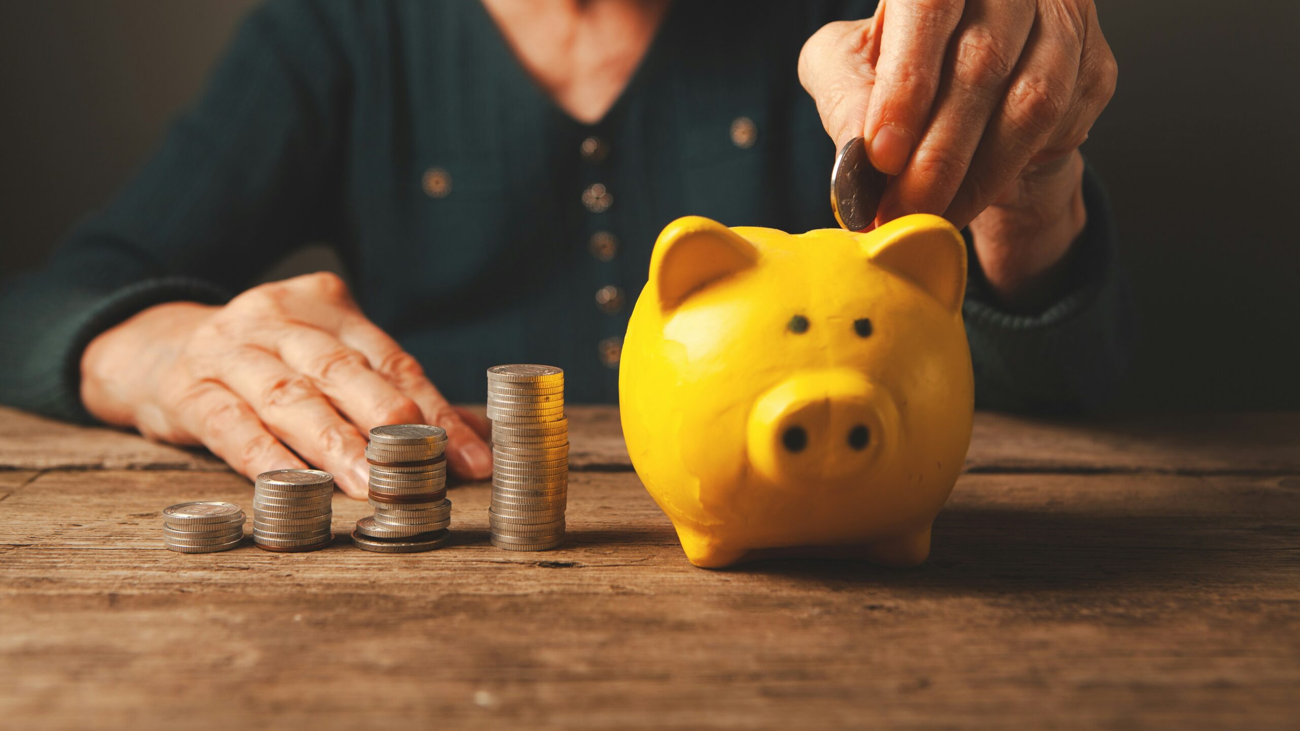 Elderly hands depositing coins into a yellow piggy bank
