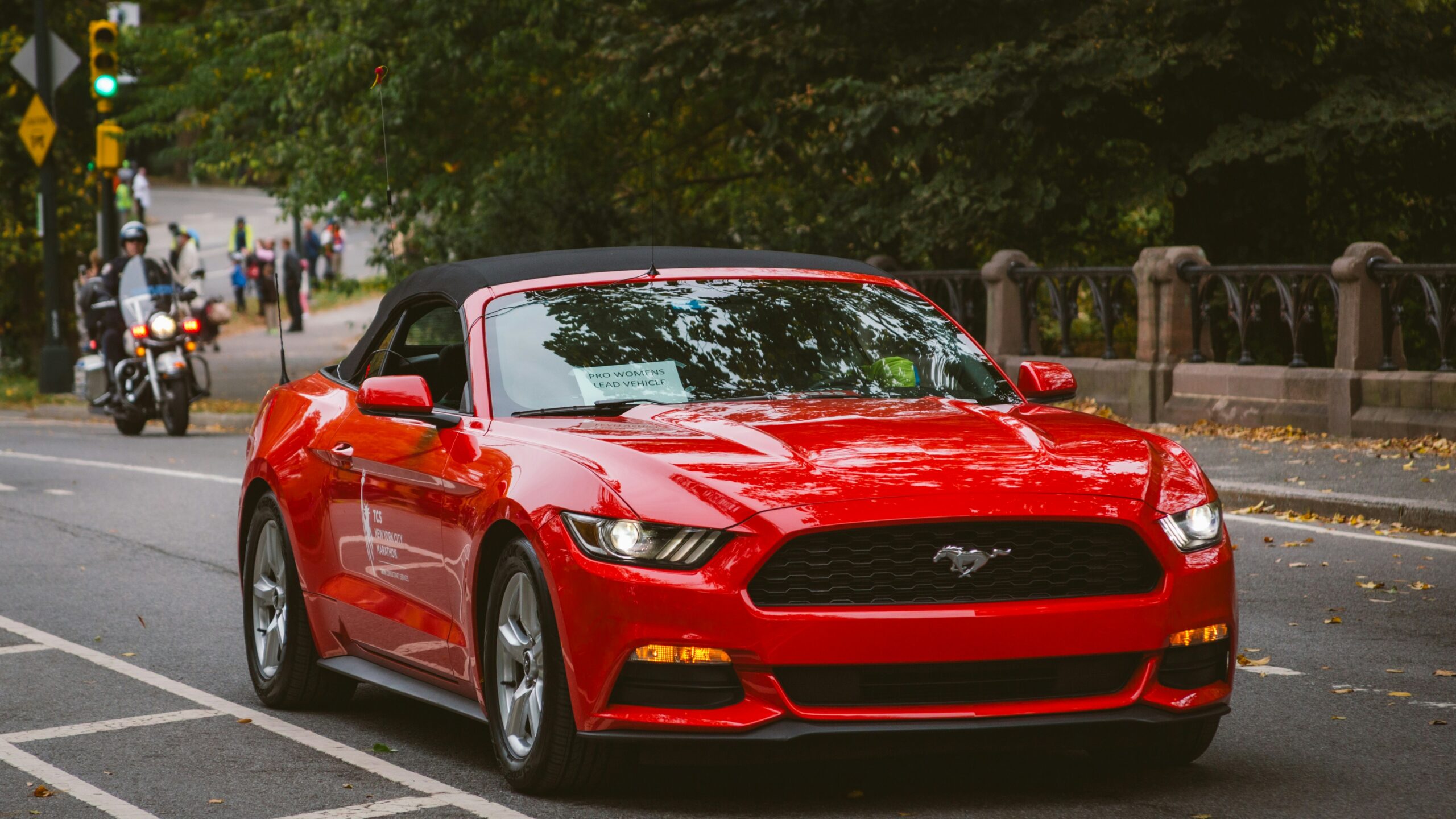 A red convertible mustang is driving down the street