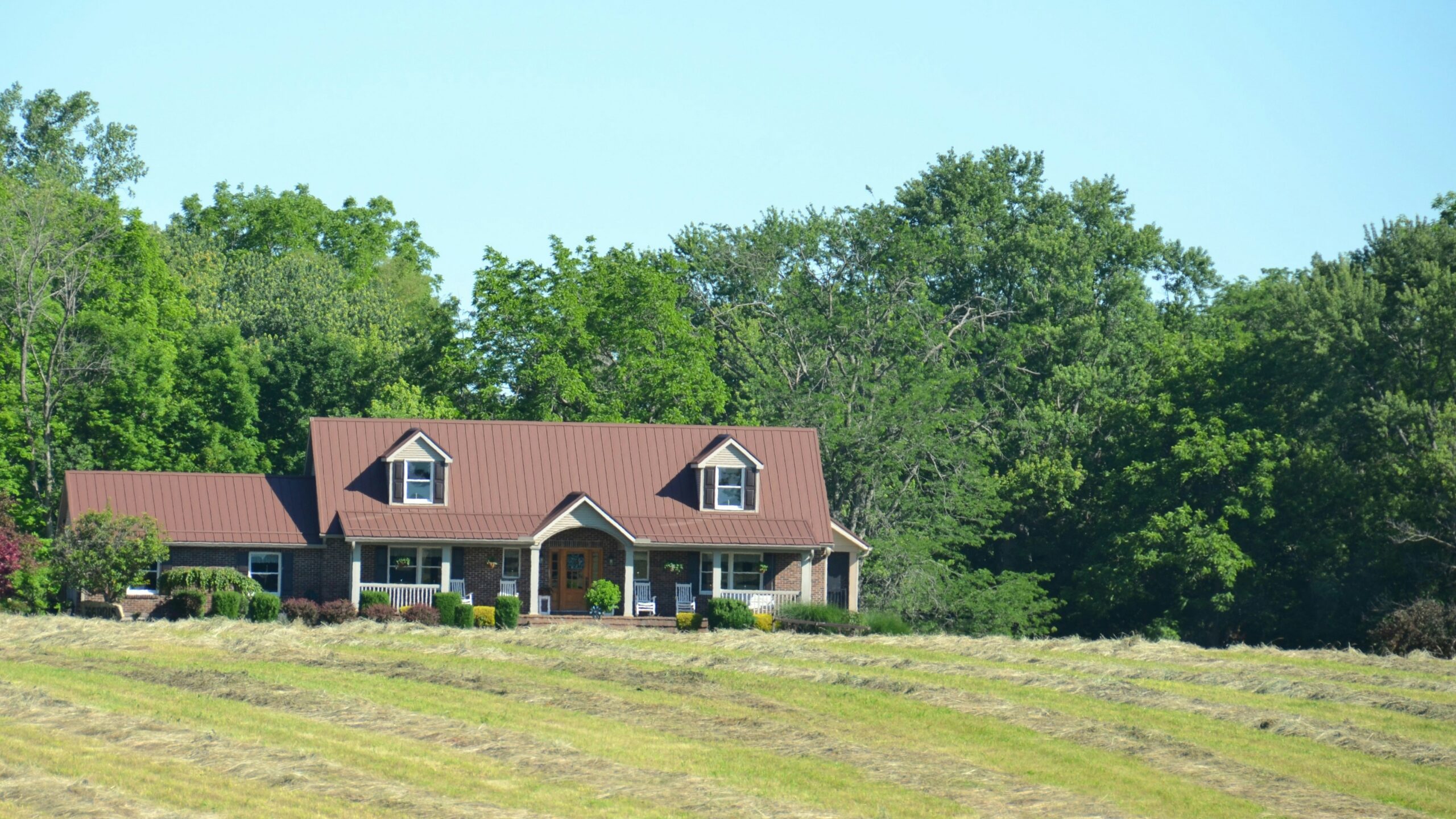 House overlooking a field with hay bales and trees
