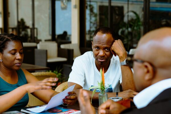 Three people discussing papers at a table in a cafe