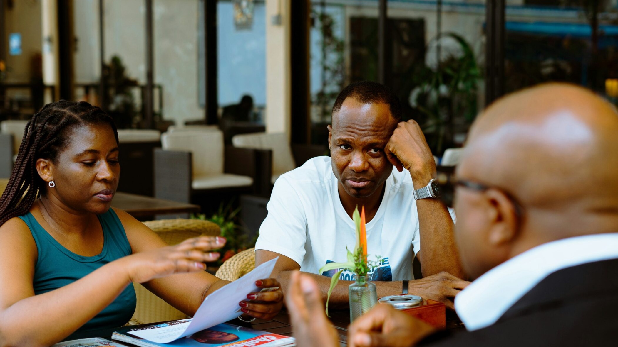 Three people discussing papers at a table in a cafe