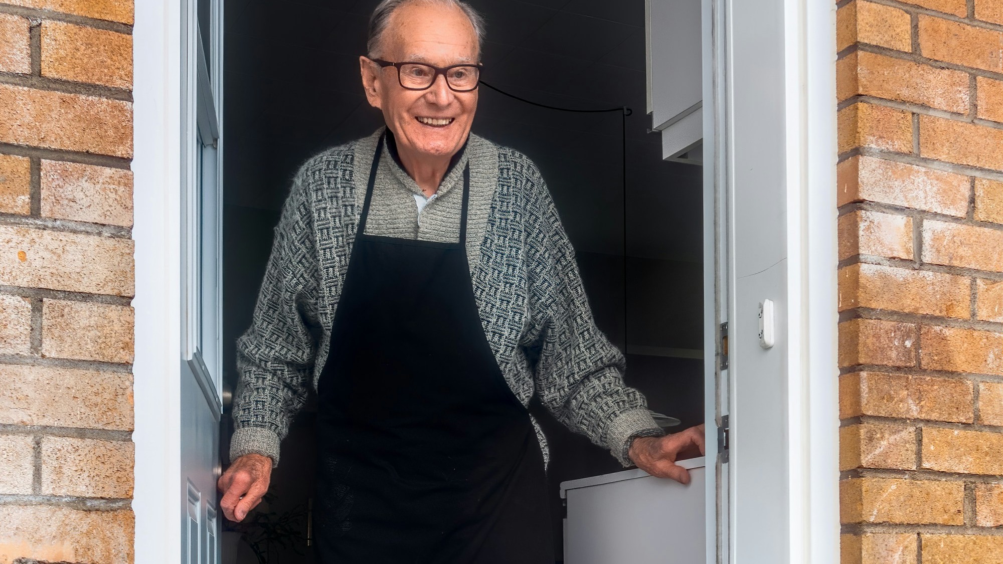 man in black vest and black dress pants standing beside white wooden door