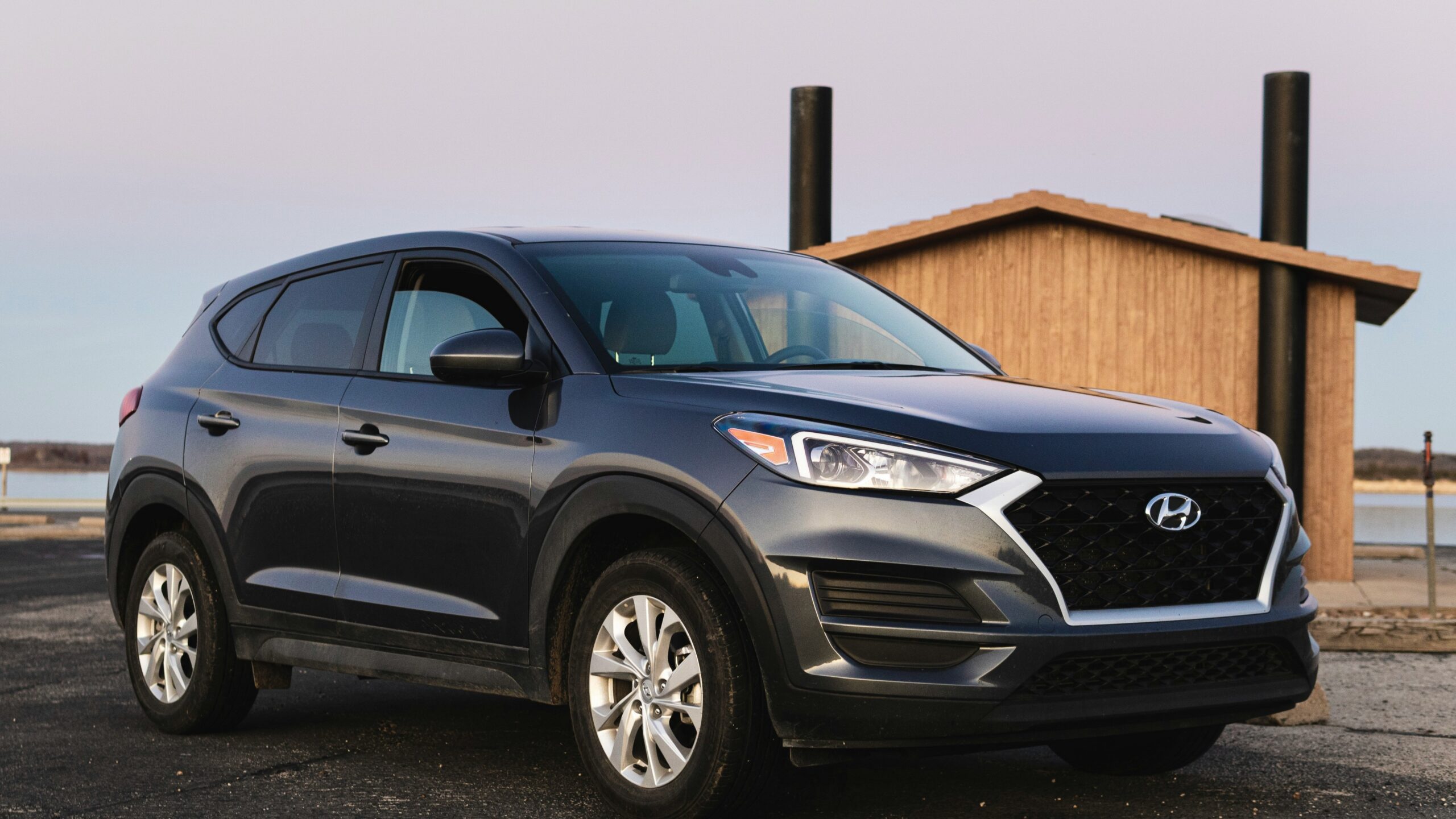 black Hyundai vehicle beside beige wooden house at daytime