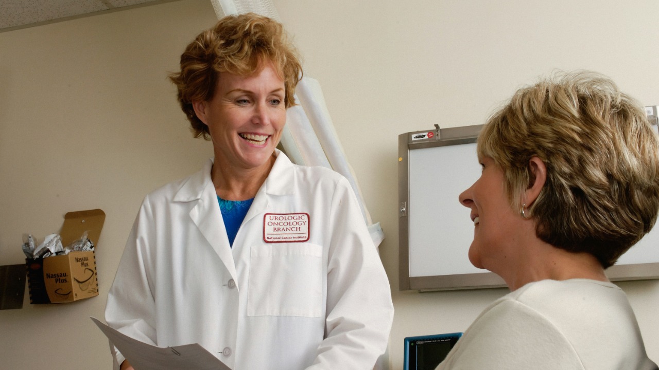 A smiling doctor in a white coat talking to a patient in a clinic