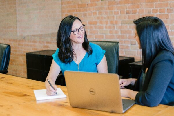 woman in teal t-shirt sitting beside woman in suit jacket