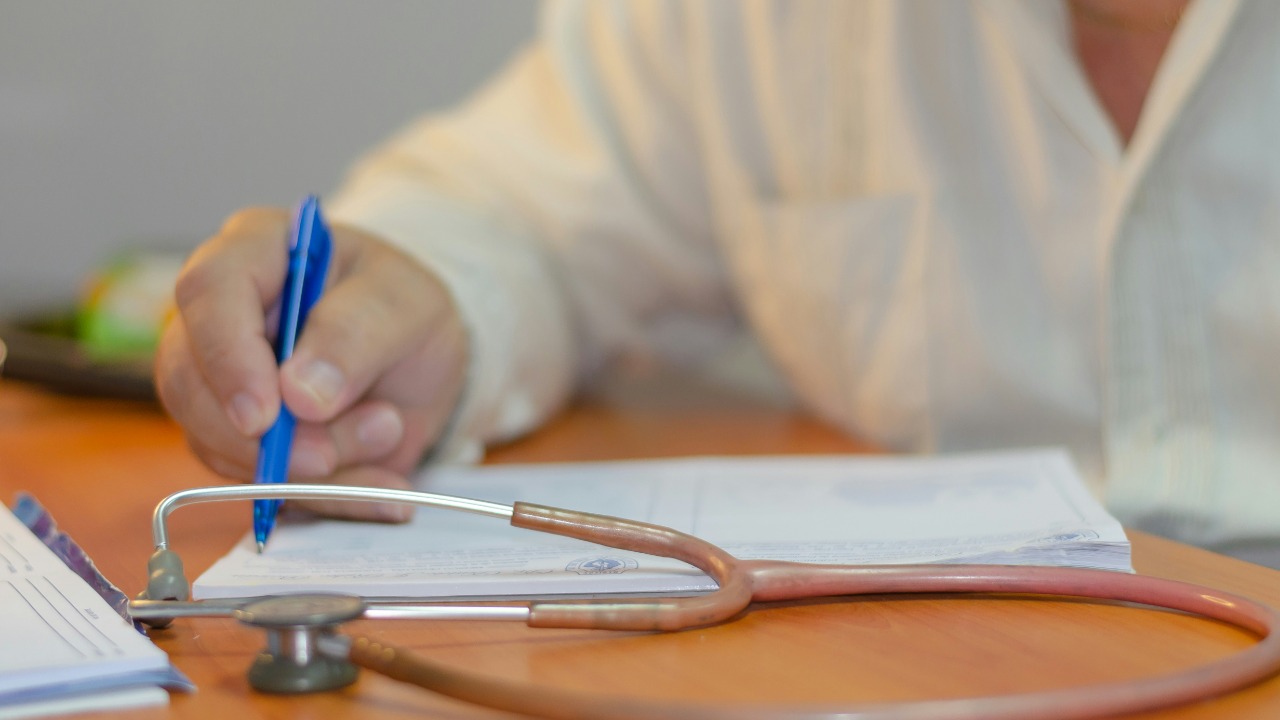 a person writing on a piece of paper with a stethoscope