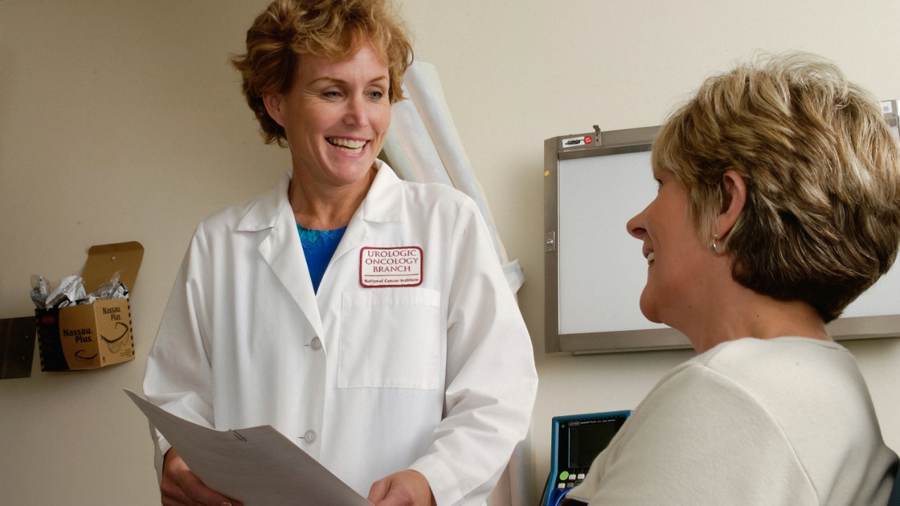 A smiling doctor in a white coat talking to a patient in a clinic
