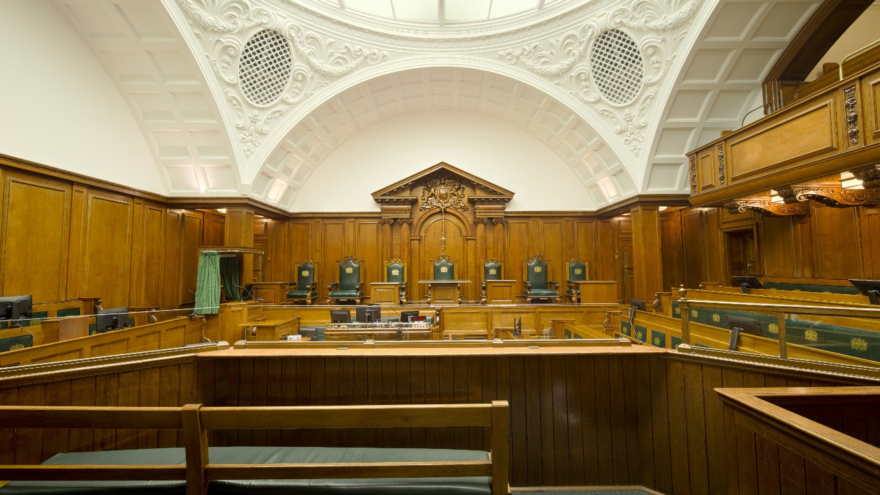 Empty courtroom featuring rich wooden paneling and a decorative ceiling