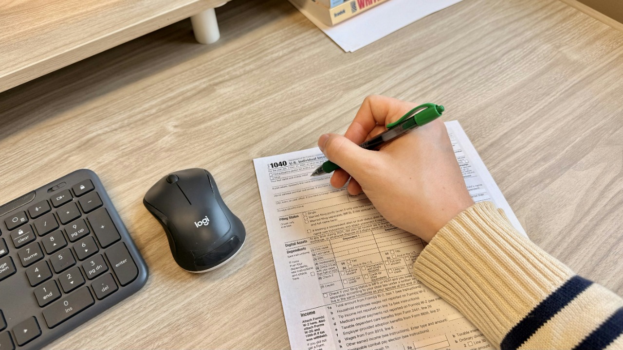 Hand writing on document next to keyboard and mouse