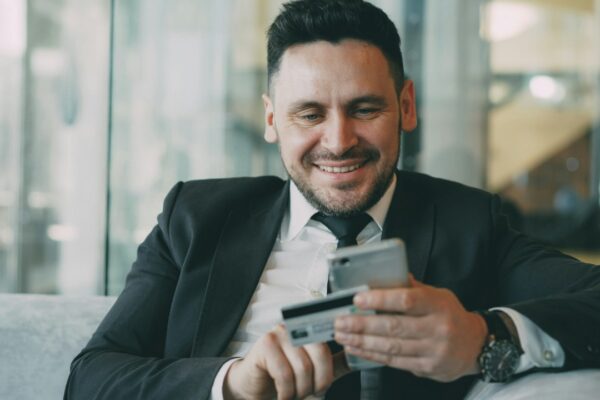 Man in suit smiling while holding phone and credit card