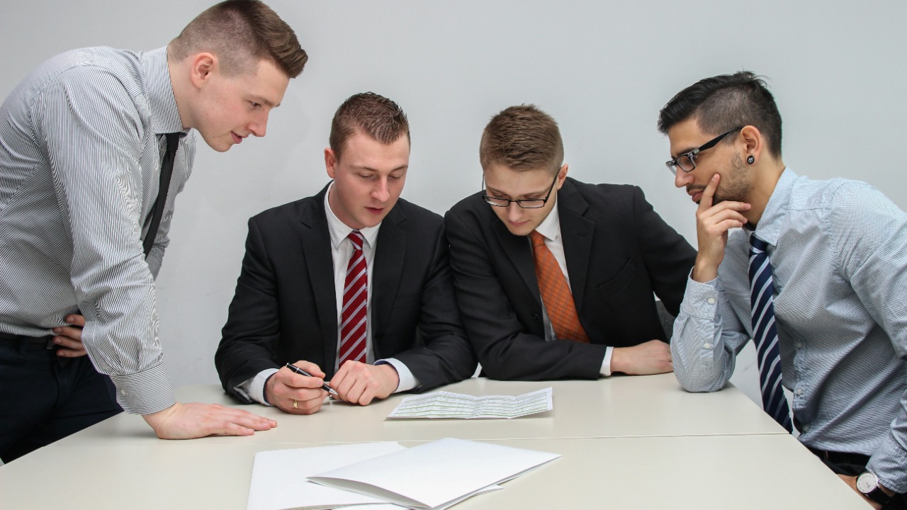 four men looking to the paper on table