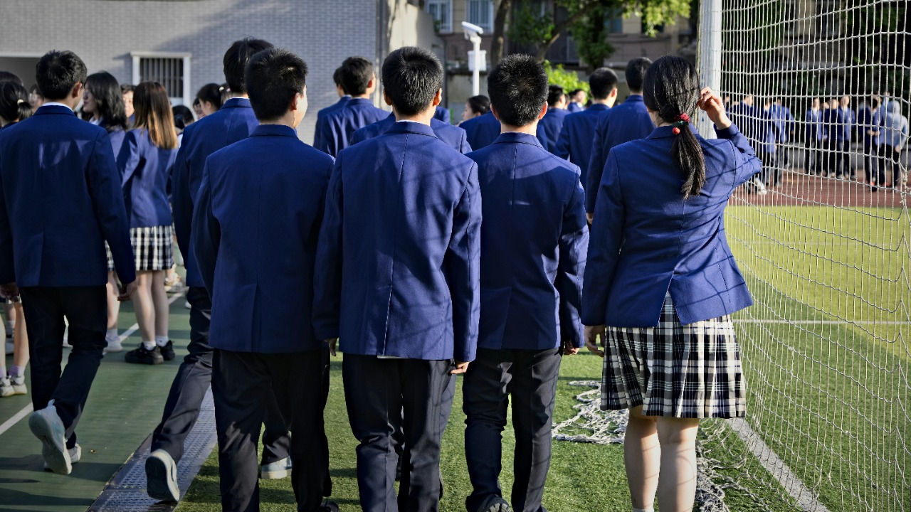 Students in uniform are walking near a sports field